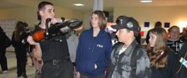 Noc Zawodowców. Hol Szkoły Podstawowej w Sierakowie. Przy stoisku Komendy Powiatowej PSP w Rawiczu znajduje się kilka osób. Strażak prezentuje nożyce hydrauliczne - trzymając je na wysokości barku. 