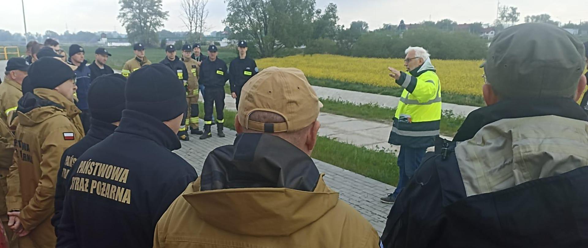 Na zdjęciu widać przedstawiciela Wód Polskich opisującego budowę polderu "Żelazna" uczestnikom szkolenia - przedstawicielom Państwowej i Ochotniczej Straży Pożarnej, Wód Polskich i Powiatowego Zespołu Zarządzenia Kryzysowego Miasta Opole.