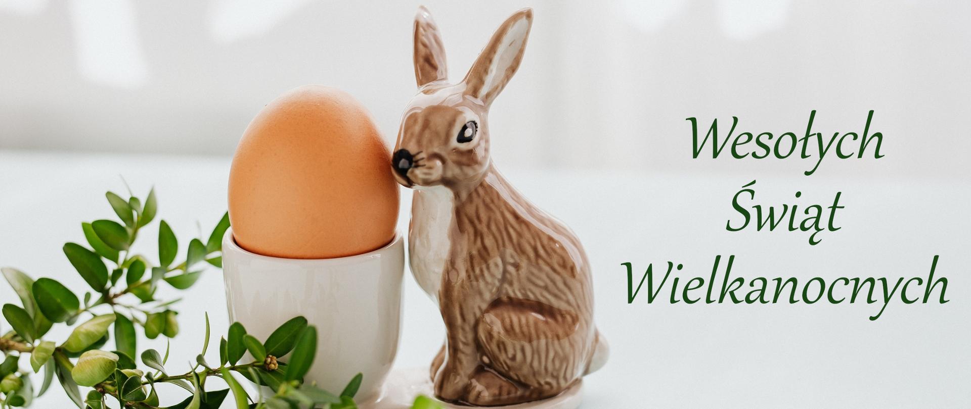 Zdjęcie przedstawia porcelanowego zająca, jajko oraz gałązkę.