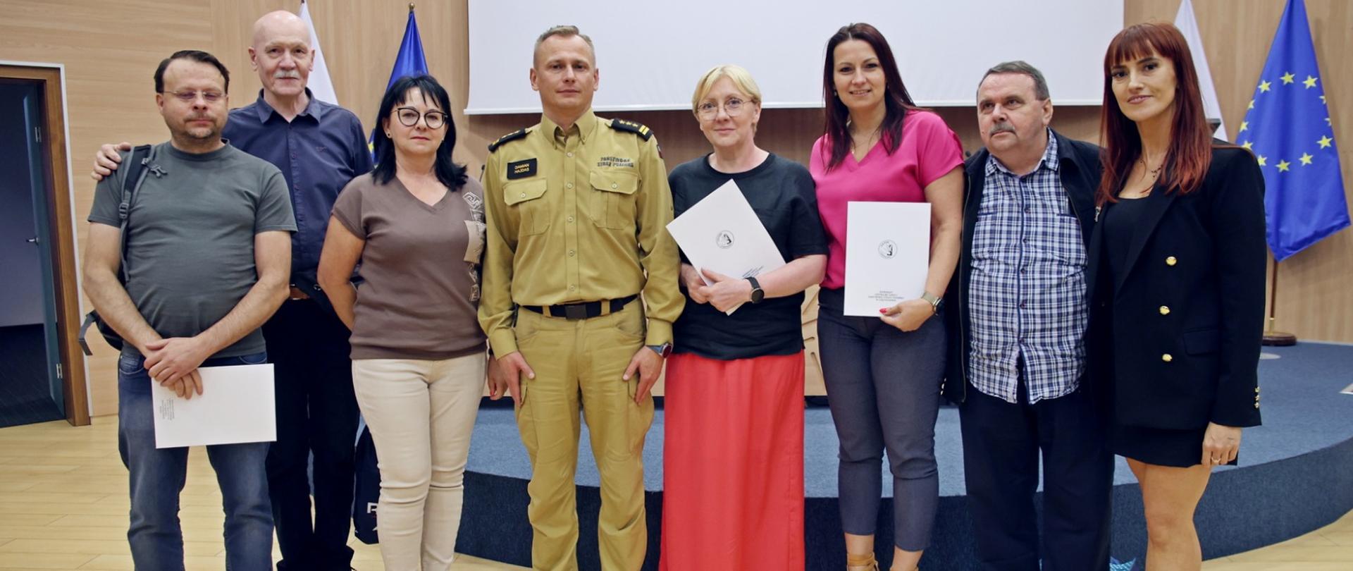 Pamiątkowe zdjęcie siedmiu osób będących uczestnikami szkolenia z zakresu ochrony ludności i obrony cywilnej dla kadry w urzędach obsługujących organy ochrony ludności w towarzystwie Zastępcy Komendanta Centralnej Szkoły PSP