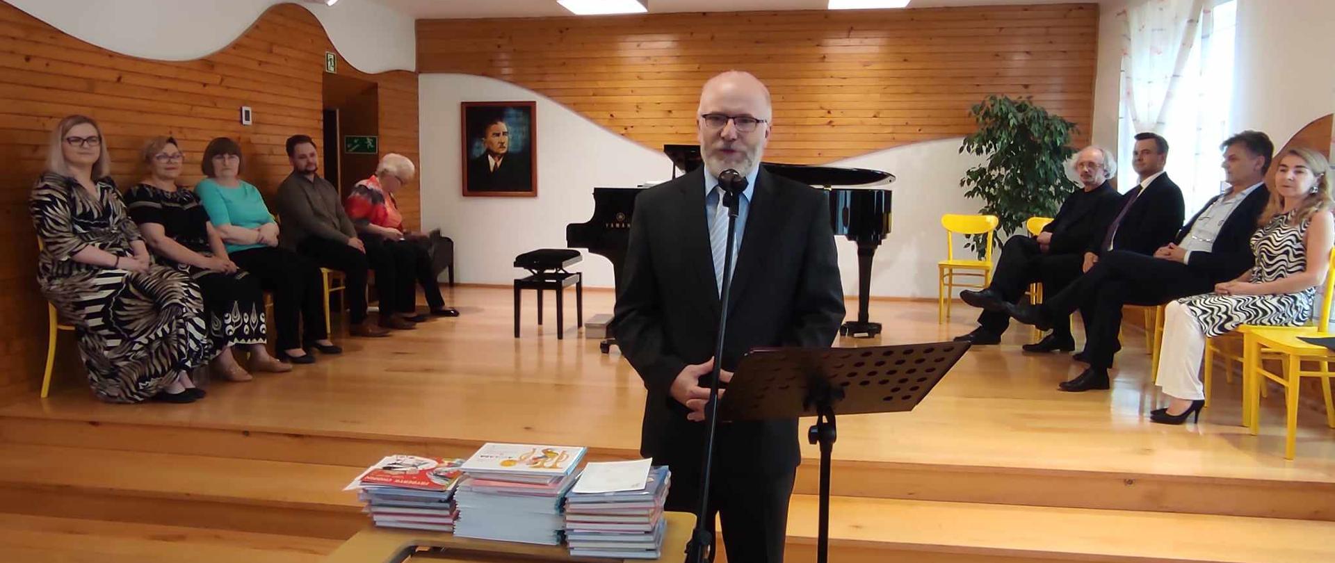 dyrektor przemawiający do uczniów na tle zgromadzonych nauczycieli