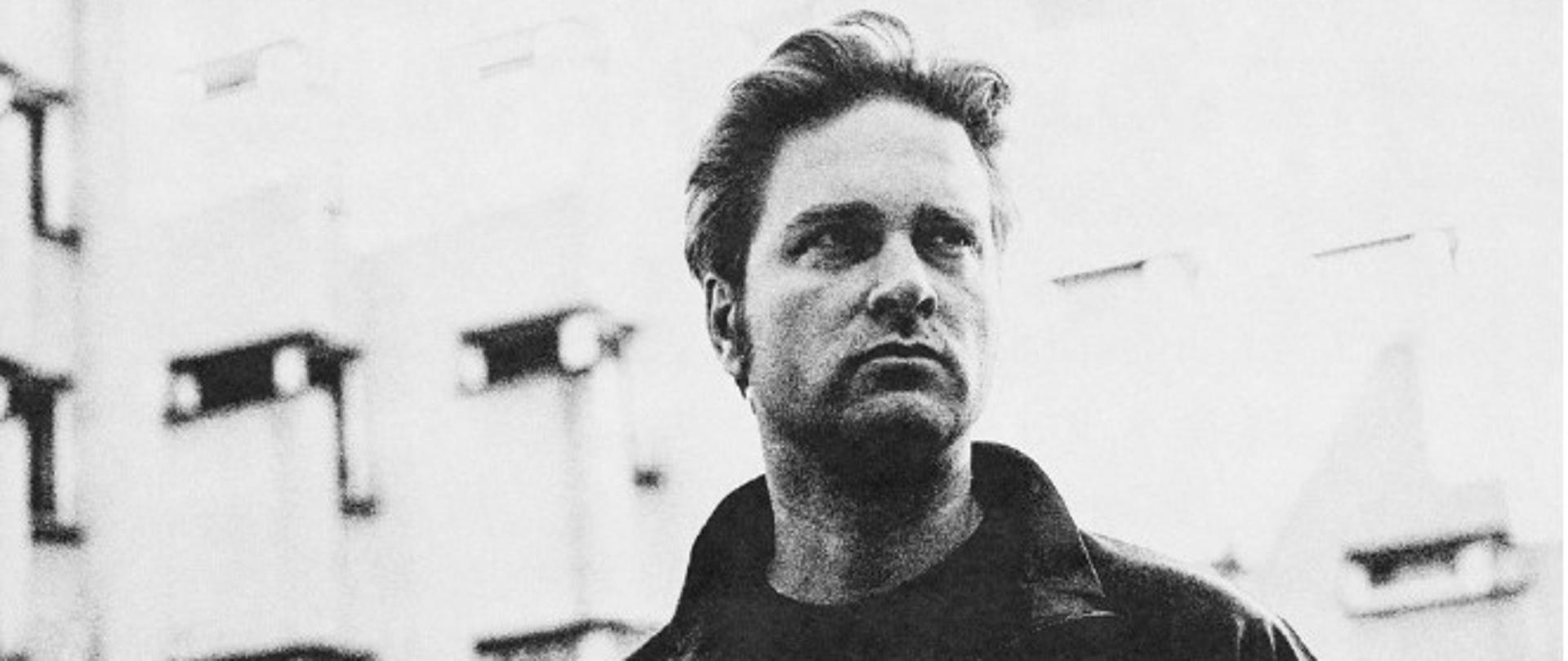 Zdjęcie Piotra Orzechowskiego w czarno-białych kolorach na tle rozmytego obiektu.