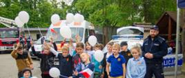Dzieci stoją w grupie przed policyjnym radiowozem i funkcjonariuszem, uczestnicząc w wydarzeniu edukacyjnym w ramach dni otwartych strażnicy