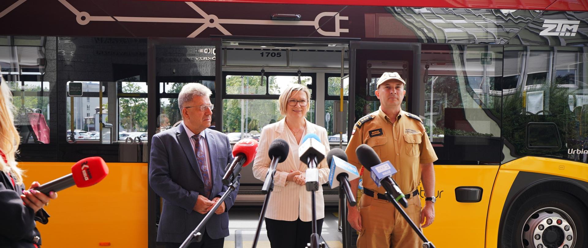 Na zdjęciu uczestnicy konferencji prasowej na tle autobusu ZTM przed nimi mikrofony różnych redakcji.