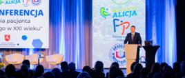 Przy mównicy stoi minister Czarnek i mówi do mikrofonu, obok niego napisy Fundacja wstawaj Alicja i Fizjoterapia Polska.
