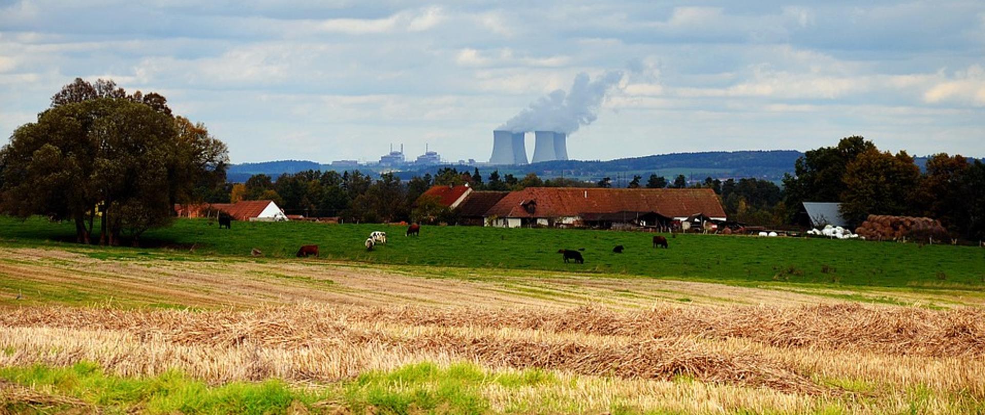 Zdjęcie przedstawiające elektrownię jądrową w Temelinie Na zdjęciu widać pole uprawne, zwierzęta gospodarskie oraz w tle w odległości kilku kilometrów elektrownię jądrową 