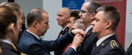 Z prawej stojący w rzędzie strażacy w mundurach wyjściowych z lewej Wicewojewoda wręczający strażakom odznaczenia