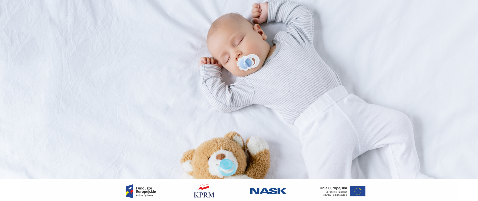 Zdjęcie ubranego na biało noworodka śpiącego na białym prześcieradle. Na dole obok dziecka - pluszowy miś.