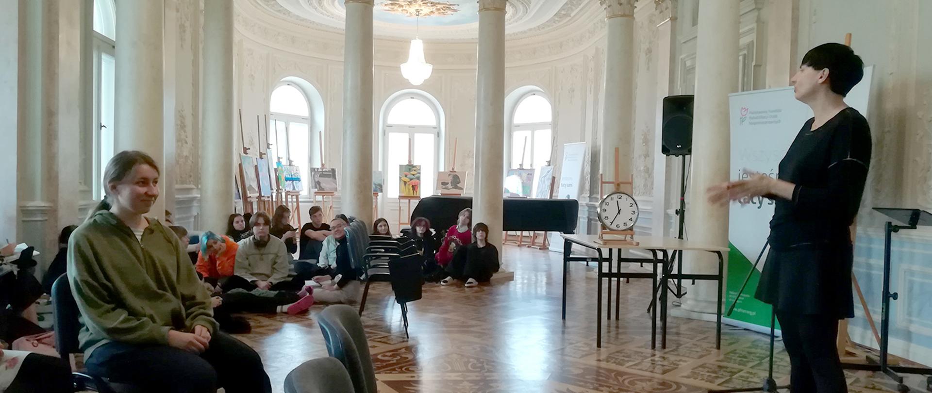 Na zdjęciu z prawej strony Pani prowadząca szkolenie na reprezentacyjnej sali w PLSP w Kościelcu. Z lewej strony zdjęcia uczniowie słuchający szkolenia.