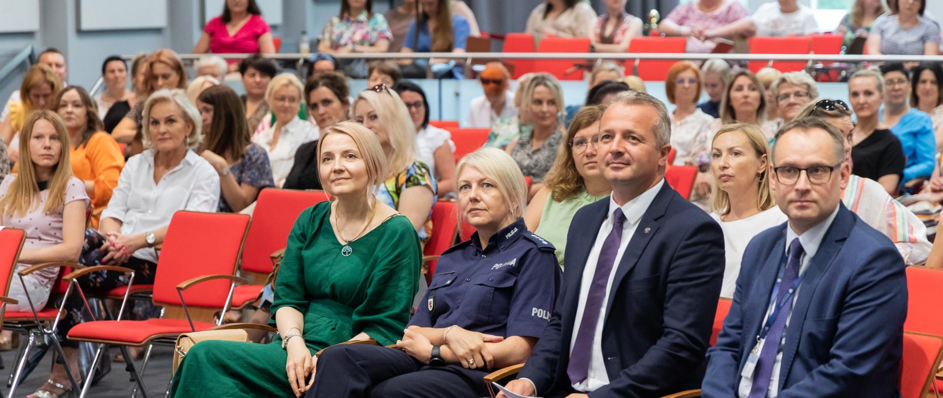 Na sali konferencyjnej uczestnicy siedzą w pierwszym rzędzie.