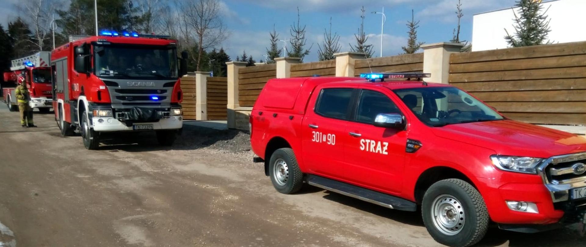 Zdjęcie przedstawia dwa samochody straży pożarnej ustawione przed posesją na której doszło do zdarzenia.