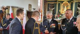 Zdjęcie przedstawia Prezesa Ochotniczej Straży Pożarnej w Gwieździnie druha Antoniego Wiśniewskiego oraz druha Mirosława Milewczyka podczas wręczania kluczyków i aktu przekazania samochodu ratowniczo- gaśniczego przez Pana Aleksandra Mrówczyńskiego - poseła na Sejm Rzeczypospolitej Polskiej, bryg. Wojciecha Berent - Zastępcę Pomorskiego Komendanta Wojewódzkiego PSP, Pana Marcina Szulc - Wójt Gminy Rzeczenica. W tle zabytkowy ołtarz kościoła w Gwieździnie. 