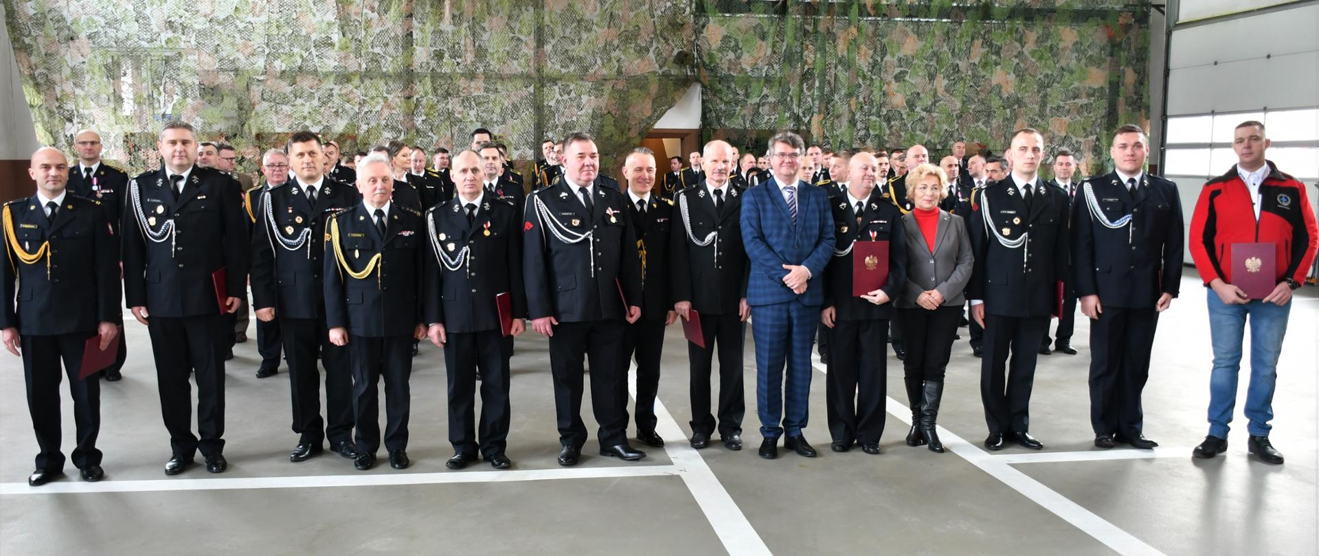Zdjęcie przedstawia pozujących do wspólnego zdjęcia druhów ochotników i zaproszonych gości w tym: Pana Maciej Wąsik - Wiceministra Spraw Wewnętrznych i Administracji, Panią Annę Cicholską - Poseł na Sejm Rzeczypospolitej Polskiej, Pana gen. brygadier Andrzeja Bartkowiaka - Komendanta Głównego Państwowej Straży Pożarnej.