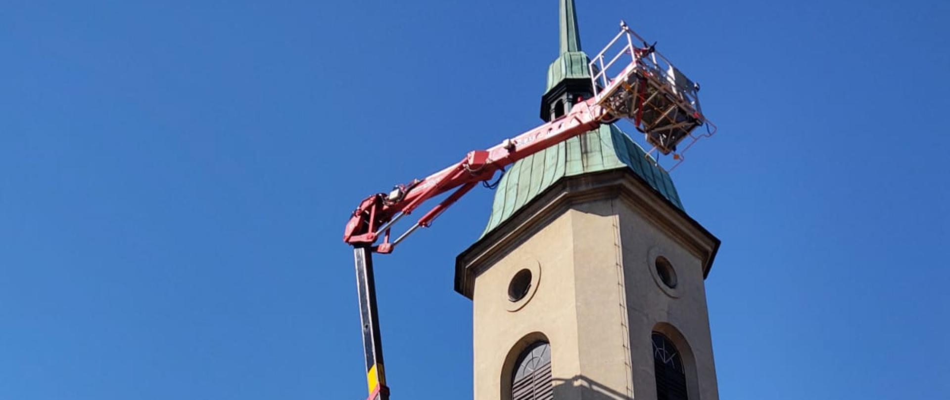 Podnośnik hydrauliczny rozłożony przed kościołem. Kosz na wysokości kopuły wieży.