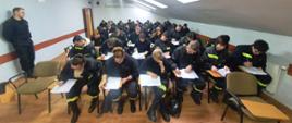 Egzamin teoretyczny. Strażacy – ochotniczy w ciemnych ubraniach koszarowych siedzą na sali egzaminacyjnej podczas pisania testu pisemnego.