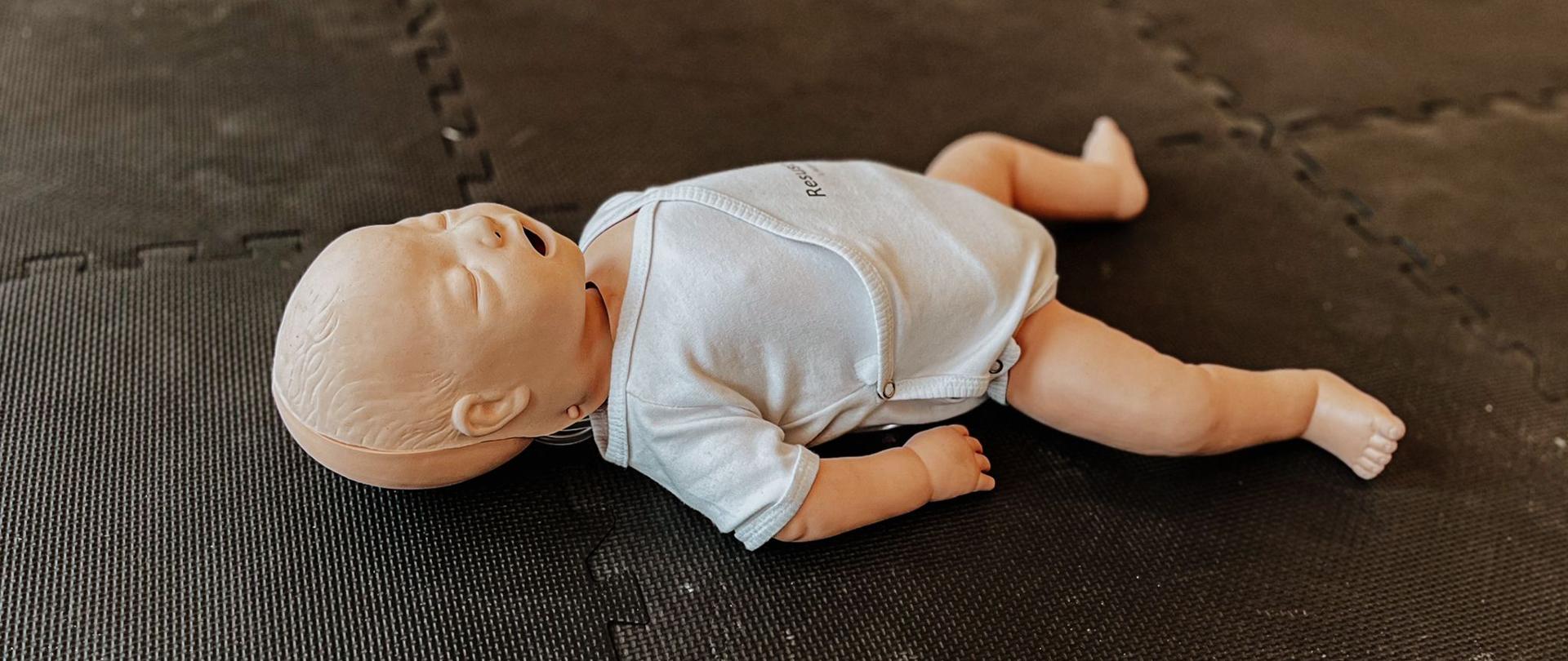 Fantom noworodka leży na macie ćwiczeniowej, zdjęcie zrobione w sali gimnastycznej budynku strażnicy