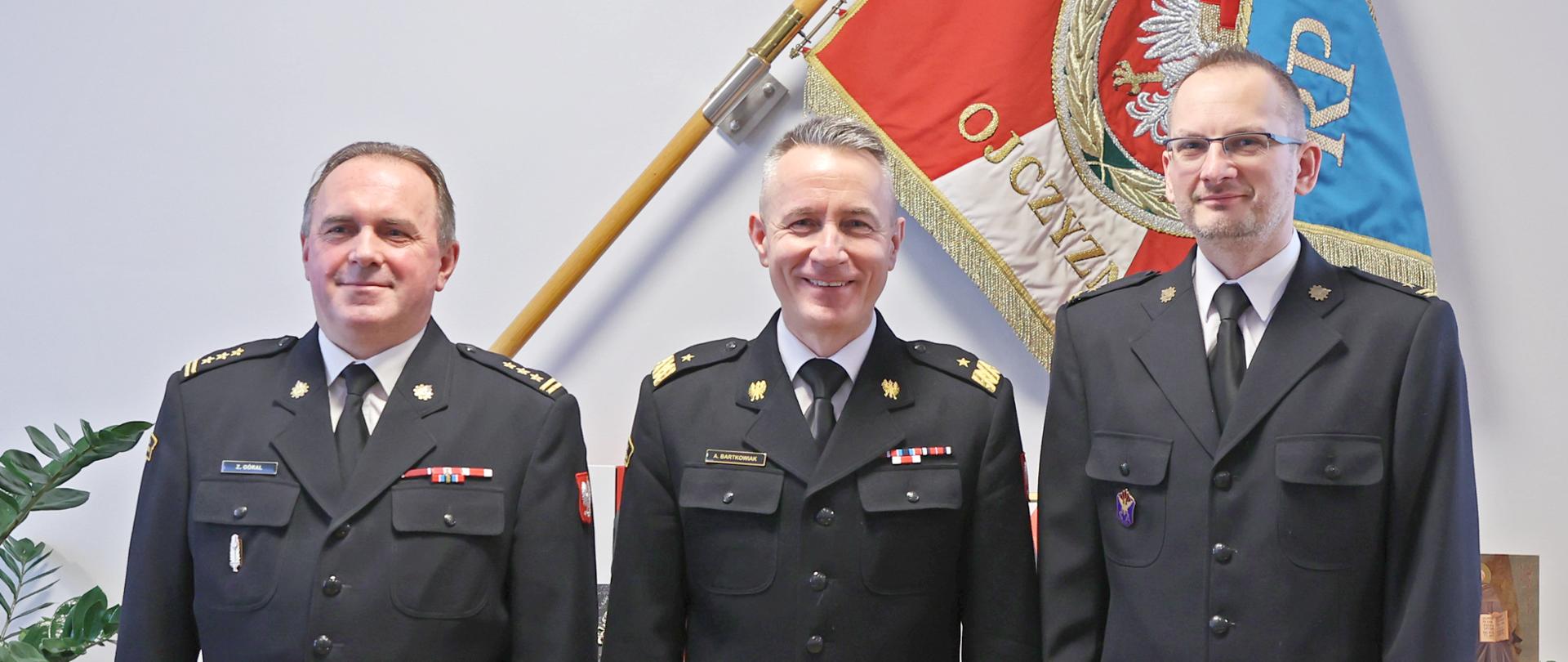 Zdjęcie pamiątkowe. Trzej mężczyźni w mundurach na tle sztandaru