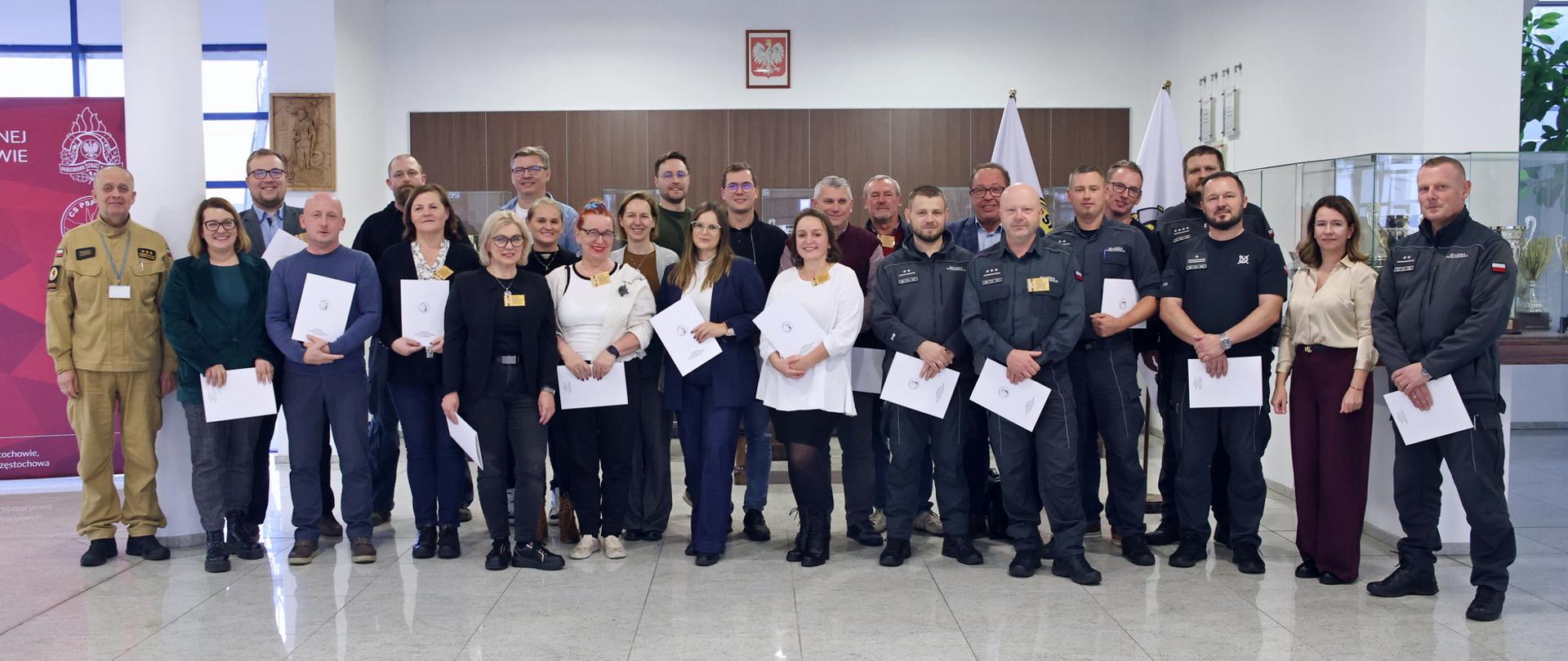 Pamiątkowe zdjęcie grupowe uczestników szkolenia inspektorów ochrony przeciwpożarowej (24 osoby) w towarzystwie oficera CS PSP oraz kobiety