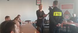 Szkolenie dla dowódców OSP.
Na zdjęciu w pomieszczeniu budynku Komendy powiatowej PSP w Ostrowcu Św. odbywa się szkolenie dla dowódców OSP z terenu OSP. Na pierwszym planie widać druhów, którzy siedząc przyglądają się jak jednej ze szkolących udziela wywiadu przed kamerą.