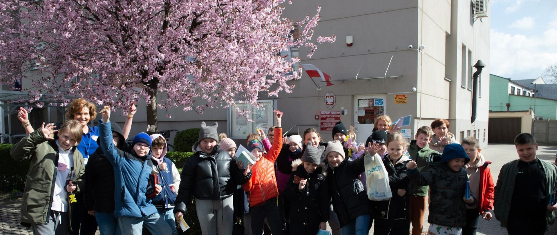 2 Dzień otwarty w Powiatowej Stacji Sanitarno - Epidemiologicznej w Krotoszynie - zdjęcie przedstawia grupę dzieci z nauczycielka i pracownikiem PSSE w Krotoszynie przed budynkiem Stacji