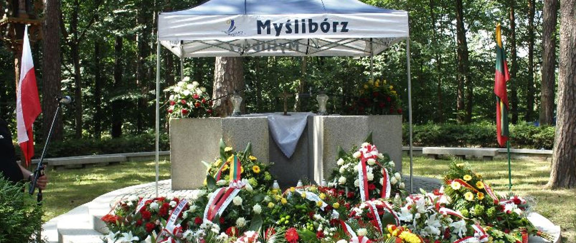 Wieńce złożone przy pomniku lotników litewskich. W tle namiot i las.