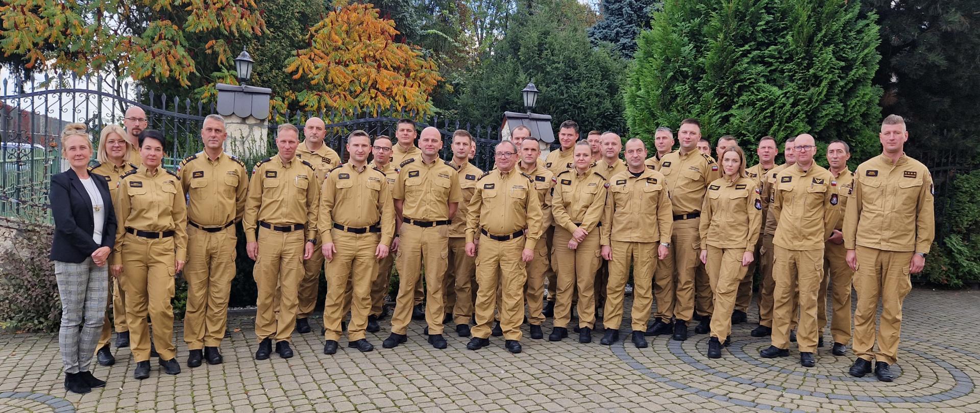 Na placu uczestnicy narady pozują do grupowego zdjęcia. Z tyłu płot i drzewa