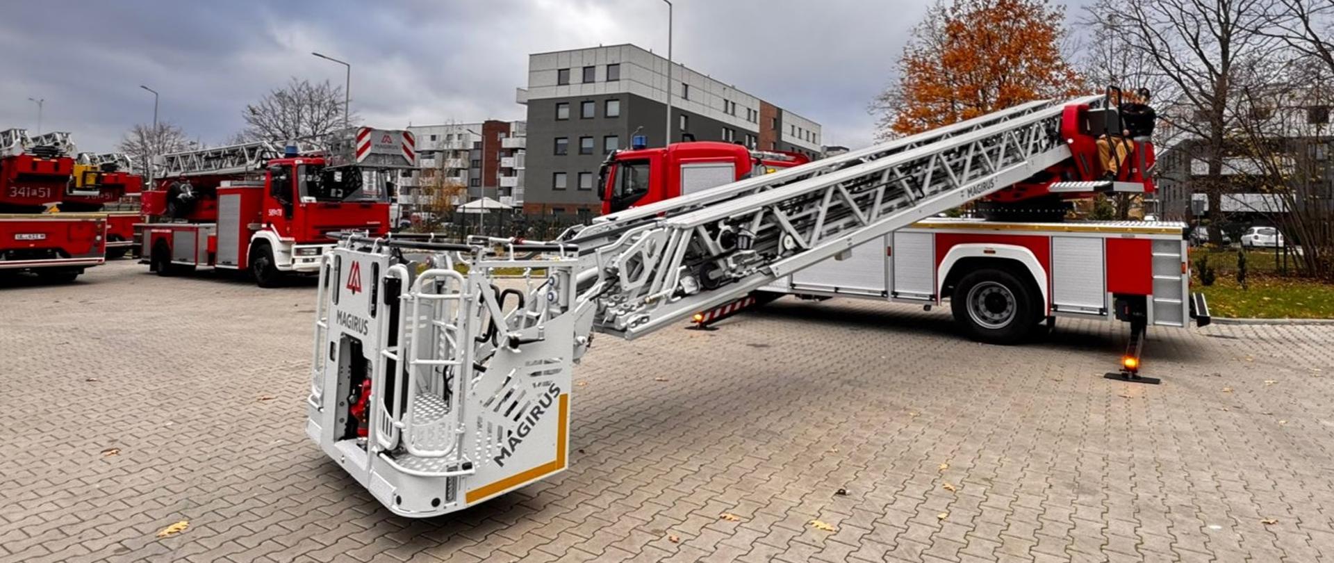 Samochód z wysuniętą w bok drabiną mechaniczną stoi na placu 