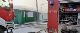 Widok samochodów ratowniczo - gaśniczych na tle budynku objętego pożarem