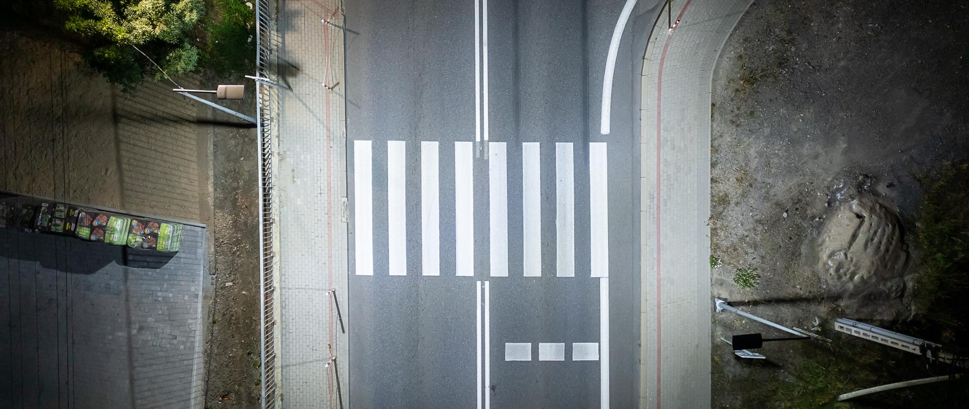 Widok na przejście dla pieszych z lotu ptaka. Zdjęcie zrobione w nocy, przejście jest oświetlone.