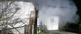 Widać wydobywający się dym z budynku oraz strażacy, którzy gaszą pożar