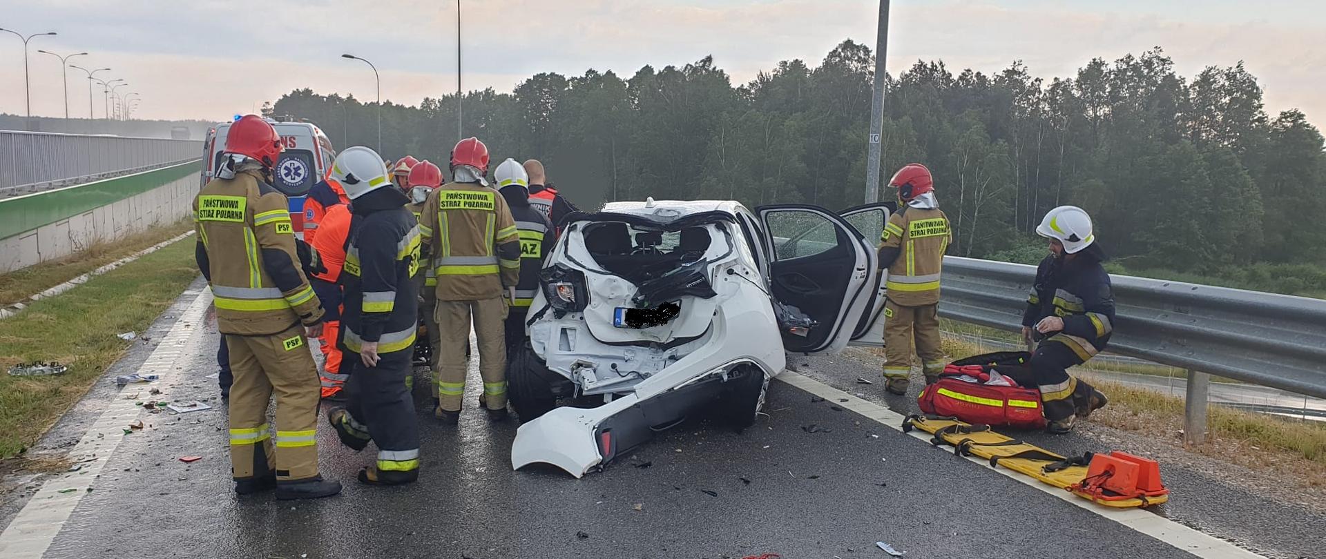Na zdjęciu widać samochód osobowy Toyota Yaris, który dachował. Obok pojazdu znajdują się strażacy i ratownicy medyczni udzielający pomocy poszkodowanemu kierowcy. 