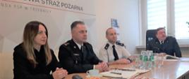 Komendant Powiatowy z Zastępca, Prezesem ZOSP RP i Starosta Powiatowym przy siedzący przy stole patrzący na ekran wideokonferencji
