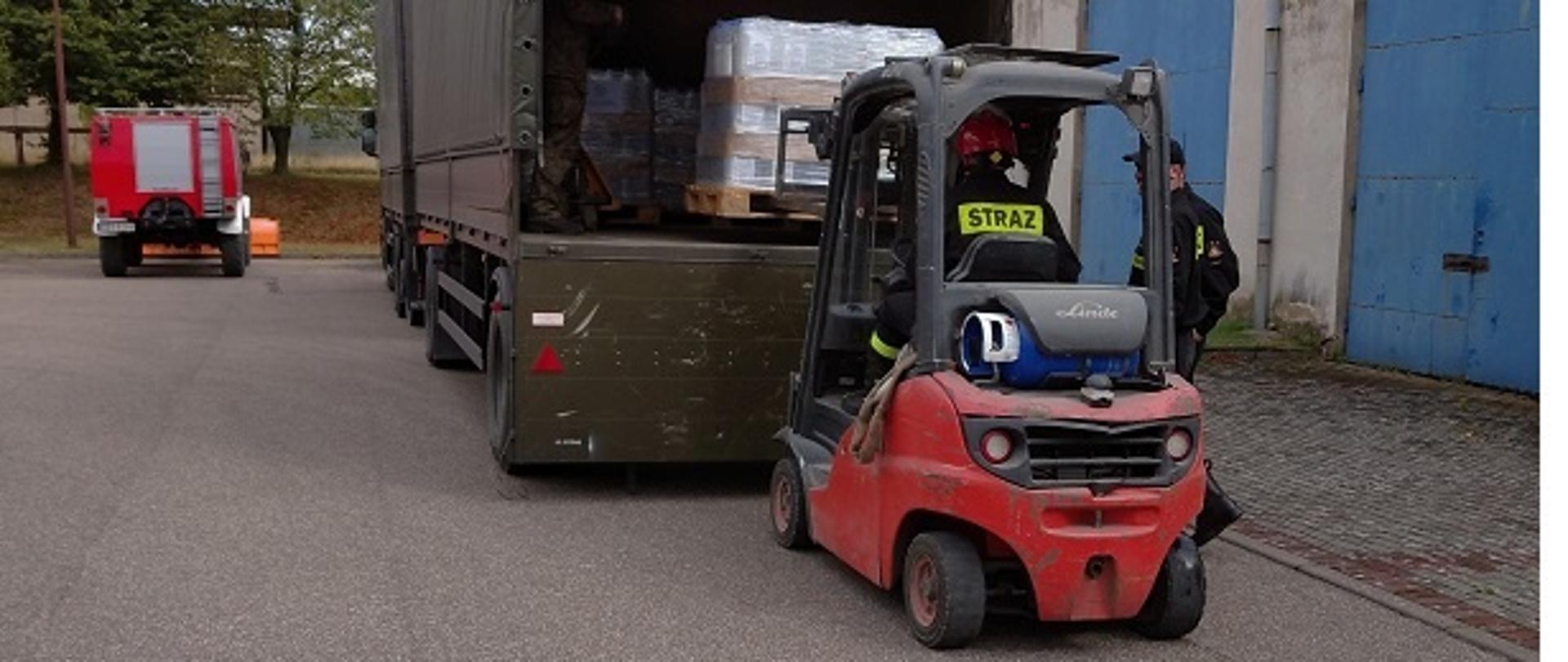 Zdjęcie przedstawia rozładunek środków ochrony indywidualnej z samochodu ciężarowego za pomocą wózka widłowego 