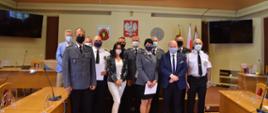 Na zdjęciu grupa ludzi pozuje do grupowego zdjęcia ustawiona w dwuszeregu. Wśród nich znajdują się policjanci, strażacy i strażnicy miejscy ubrani w galowe mundury.