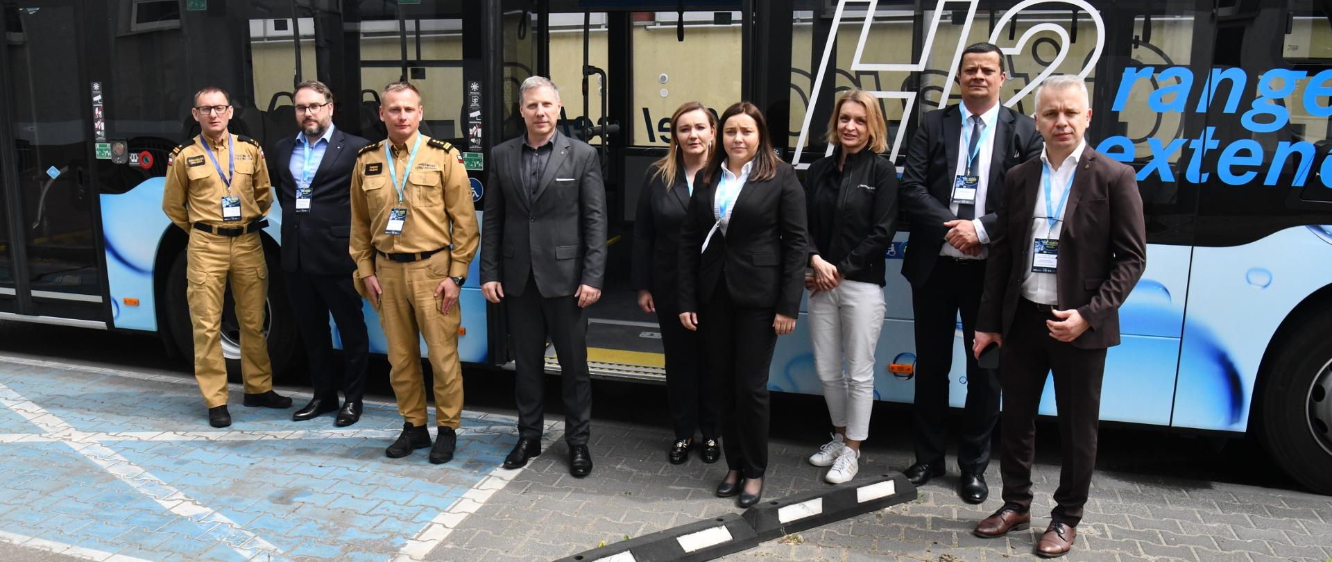 Osoby pozujące do wspólnego zdjęcia na tle autobusu zasilanego wodorem
