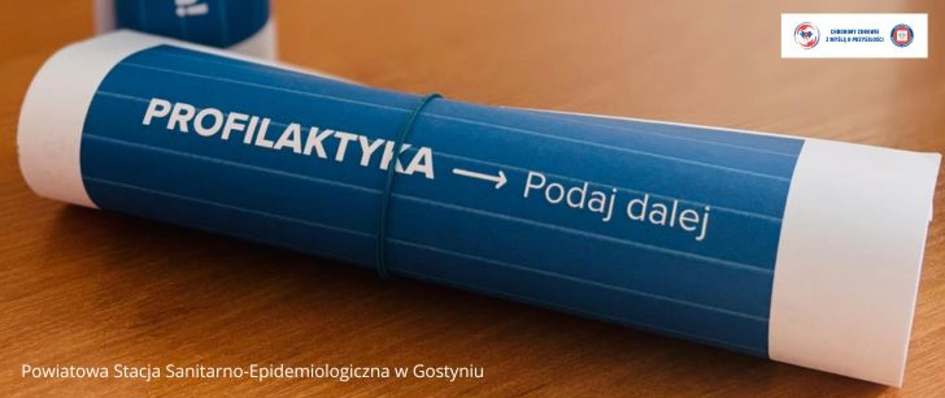 Zwinięta w rulon kartka, na kartce na niebieskim tle napis: Profilaktyka -> Podaj dalej