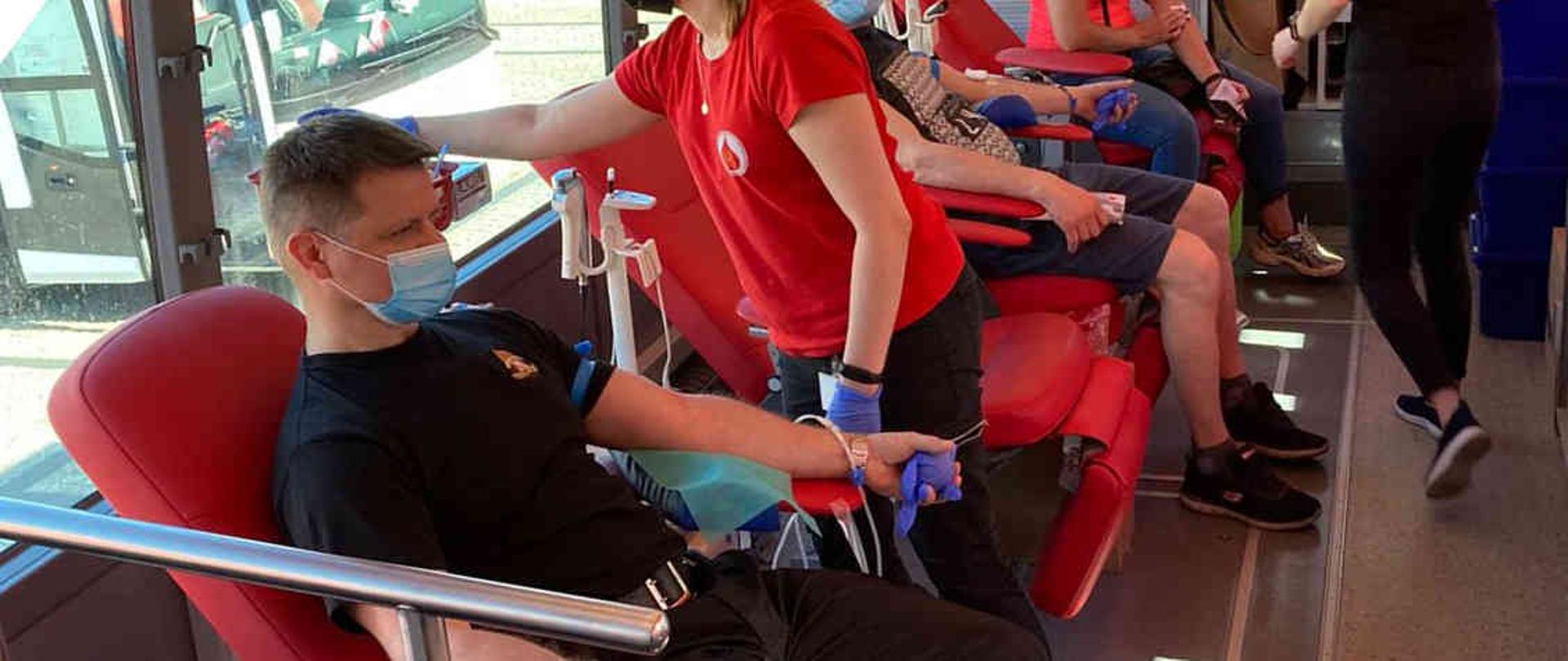 Strażak siedzący w krwiobusie i oddający krew.