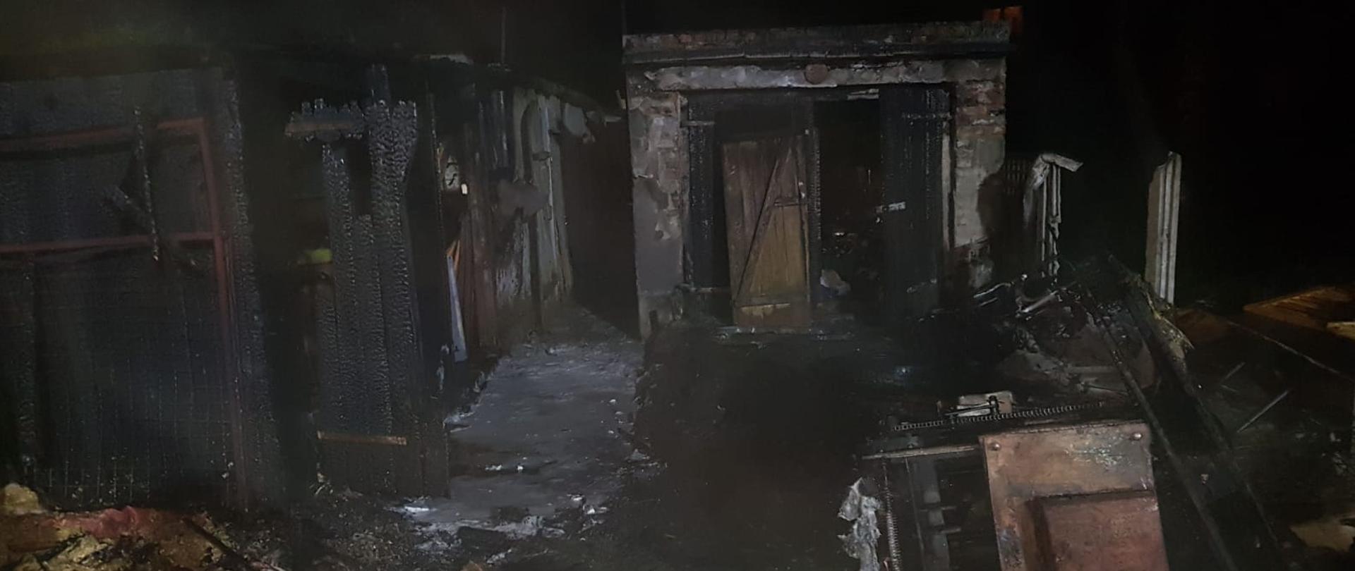 Spalone budynek gospodarczy oraz przyczepa samochodowa. Na ziemi drewniane resztki po pożarowe.