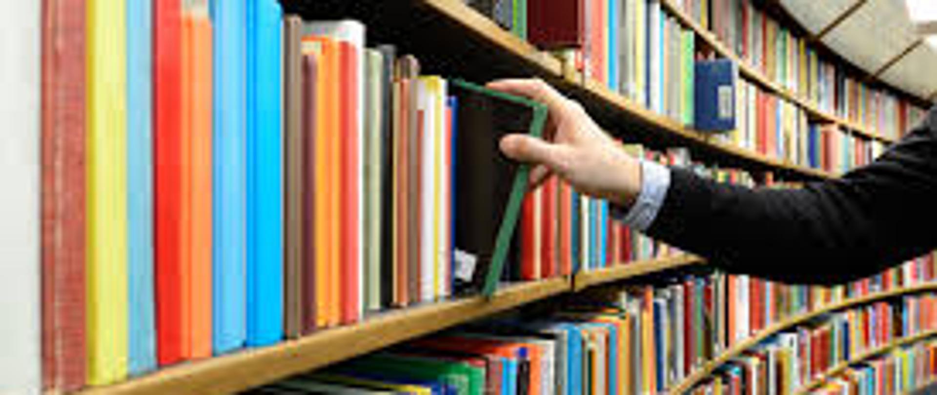 Ręka sięgająca po jedną z książek na regale