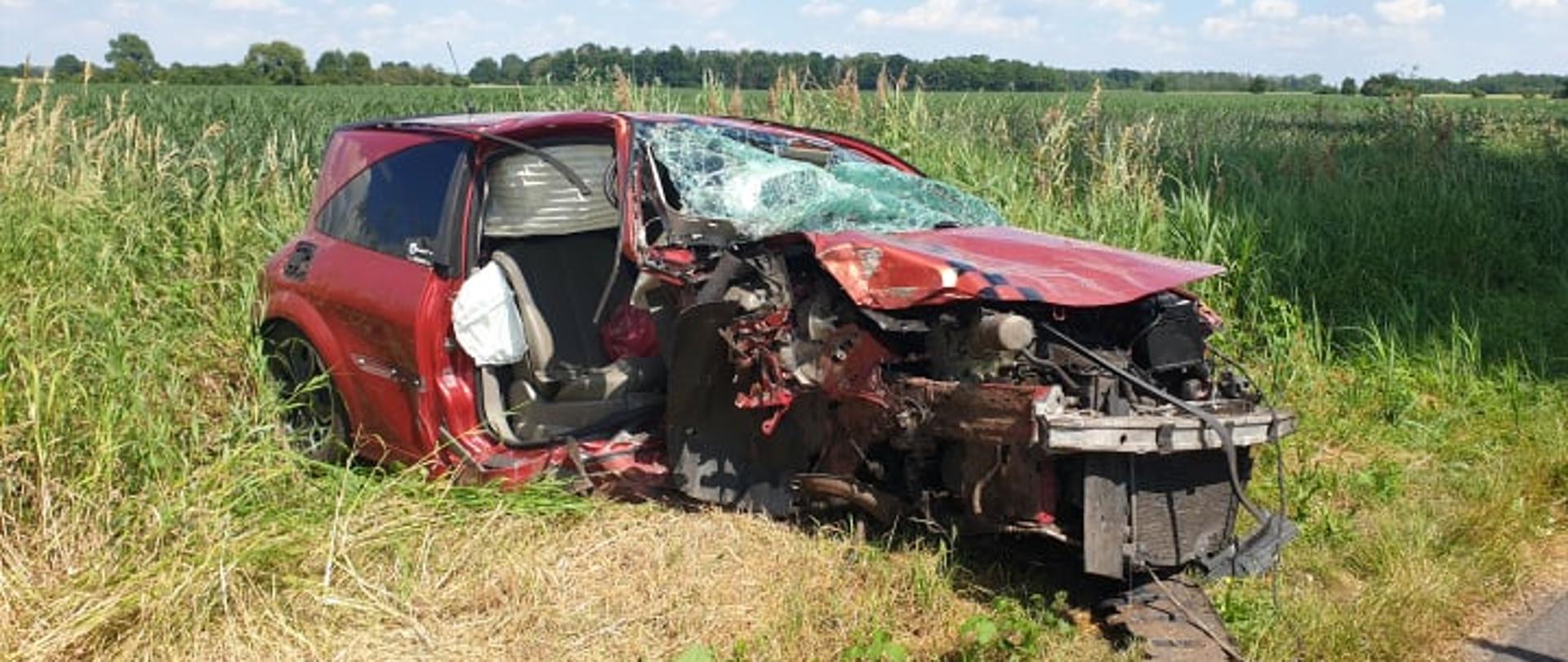 Zdjęcie przedstawia rozbity samochód marki Renault Megane znajdujący się na poboczu drogi. 