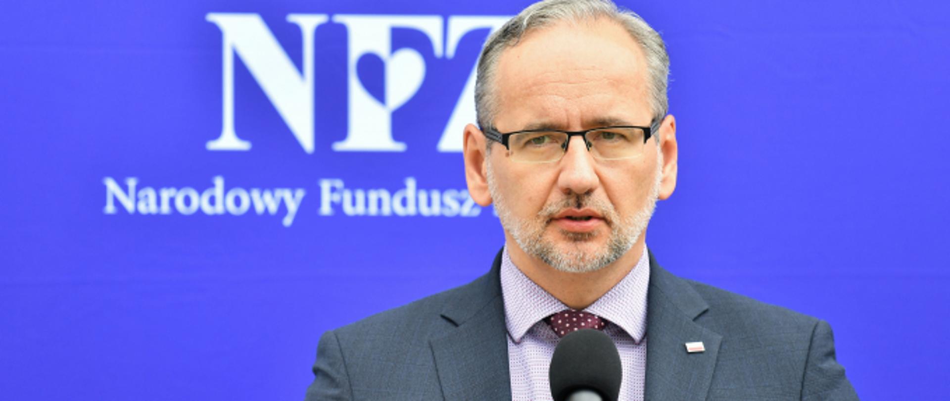 Zdjęcie przedstawiające Ministra Zdrowia, Pana Adama Niedzielskiego pozującego do zdjęcia na tle logo Narodowego Funduszu Zdrowia