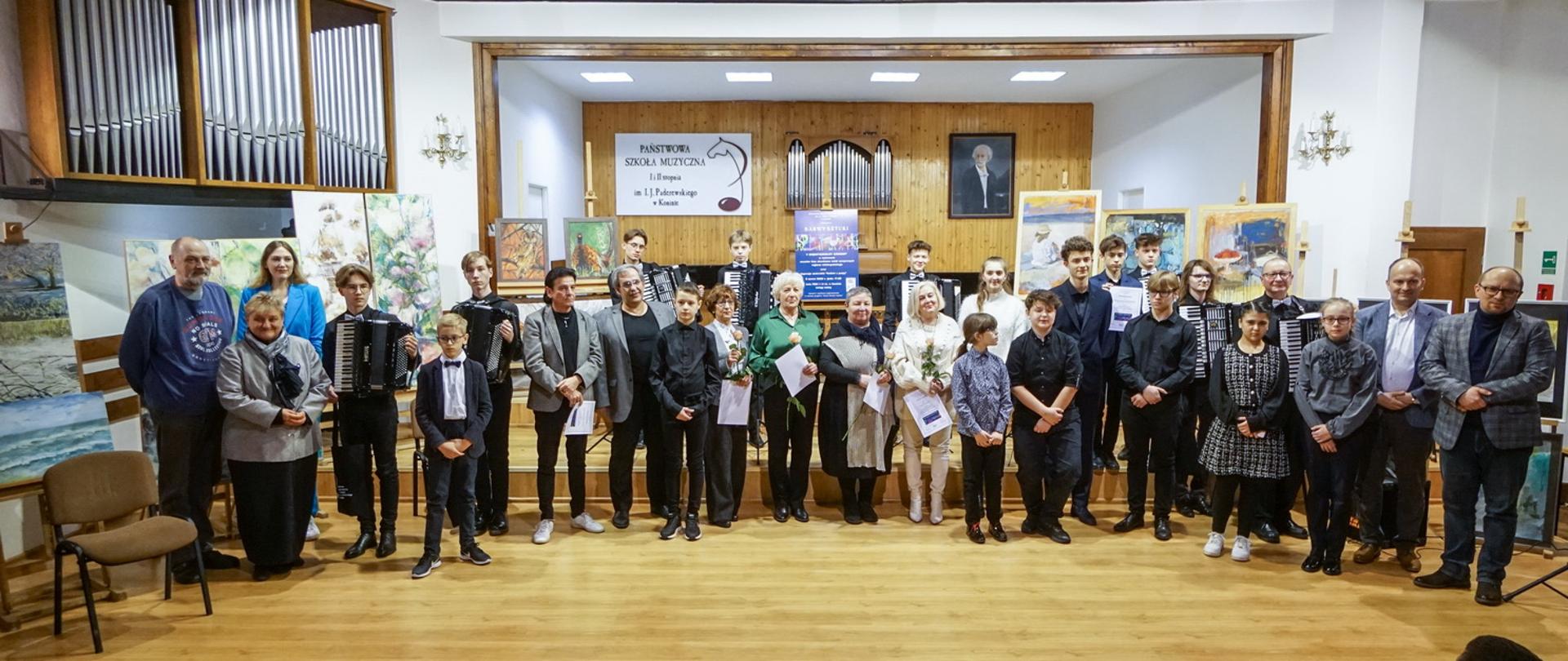 Uczestnicy wydarzenia na scenie PSM w Koninie, w tle obrazy.