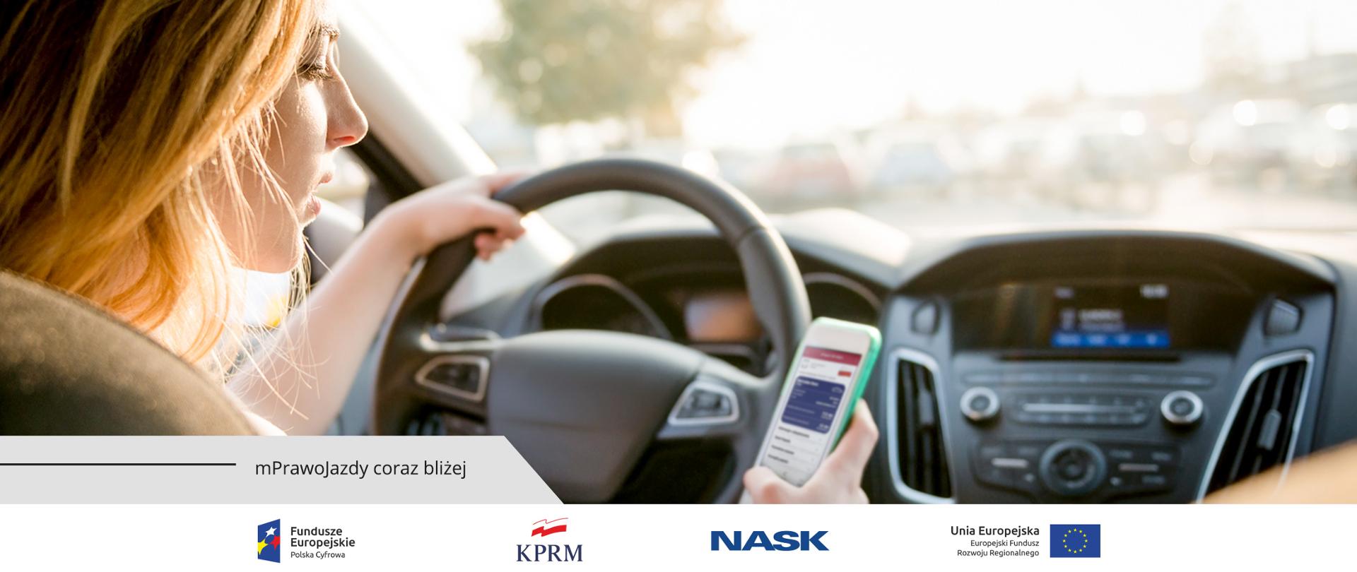 Kobieta w samochodzie, siedzi na miejscu kierowcy. Lewą ręką trzyma kierownicę, w drugiej trzyma smartfona, na którym wyświetla się mPrawo Jazdy.