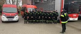 Na zdjęciu widać grupę 16 strażaków. W tle znajdują się dwa samochody straży pożarnej.
