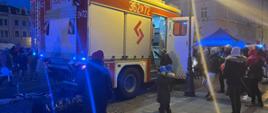 samochód pożarniczy w trakcie pokazu sprzętu, wokół zgromadzeni ludzie w tle widoczne kamienice