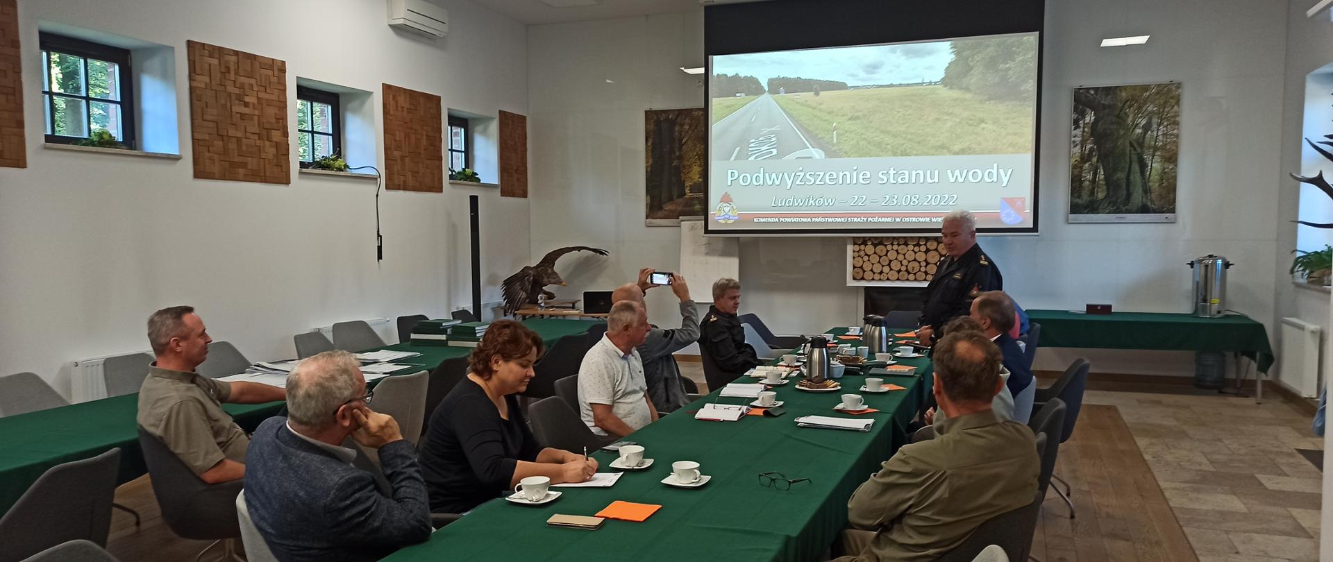 Komendant powiatowy przemawia do ludzi siedzących przy stole.
