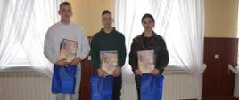 OTWP w Sobiałkowie. Świetlica wiejska w Sobiałkowie. Zwycięzcy w najstarszej grupie wiekowej pozują do wspólnego zdjęcia. Dziewczyna i dwóch chłopaków trzymają w rękach dyplomy oraz niebieskie torby z upominkami.