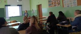 zdjęcie przedstawia osobę prowadzącą pogadankę dla grupy młodzieży w sali lekcyjnej