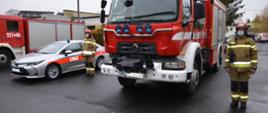 Zdjęcie przedstawia dwa średnie samochody bojowe straży pożarnej i jeden samochód operacyjny stojący na placu przy Komendzie Powiatowej Państwowej Straży Pożarnej w Wieluniu, obok pojazdów stoją kierowcy w strojach bojowych