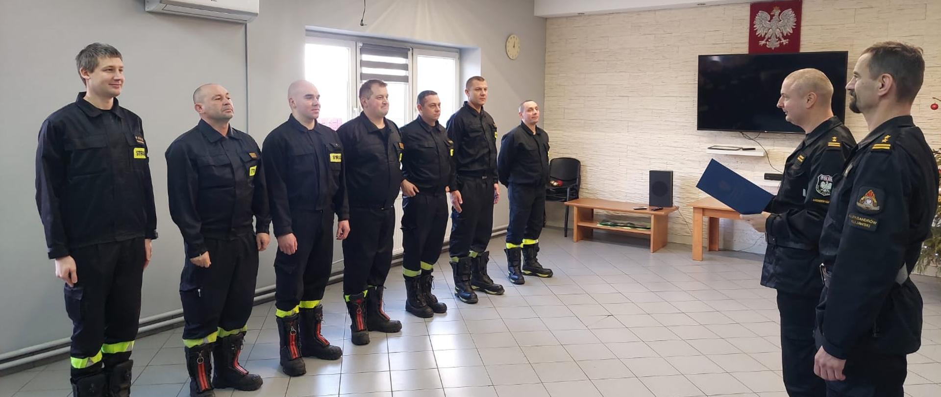 strażacy w umundurowaniu koszarowym stojący w szeregu podczas zbiórki z komendantem powiatowym. 